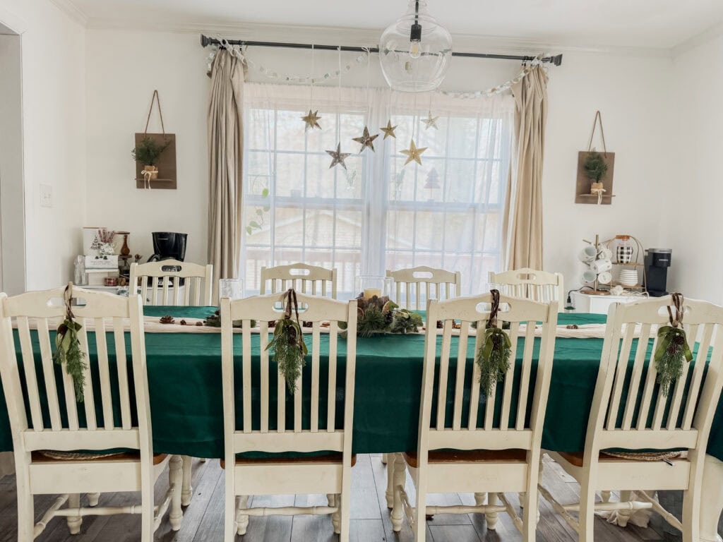 Festive holiday dining room decorated for Christmas with a long table, green tablecloth, garland, and ornaments, featuring cozy and elegant holiday home decor for family gatherings.