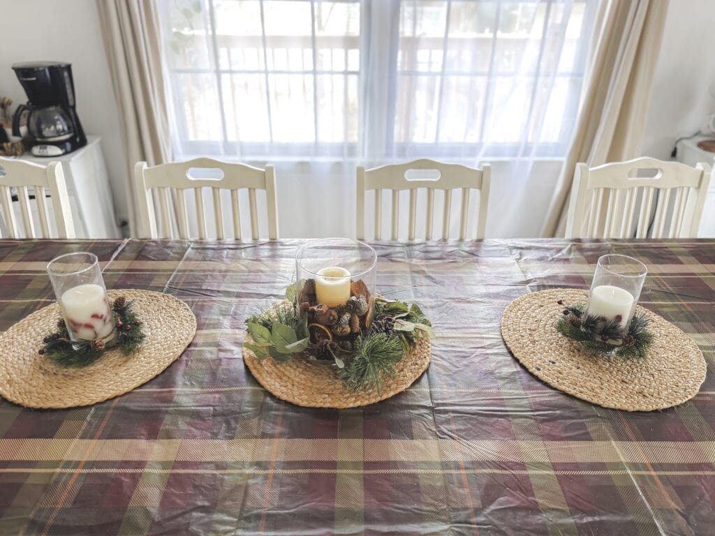 Festive holiday dining table with candle centerpieces, pinecones, and greenery, decorated for Christmas or winter celebrations.
