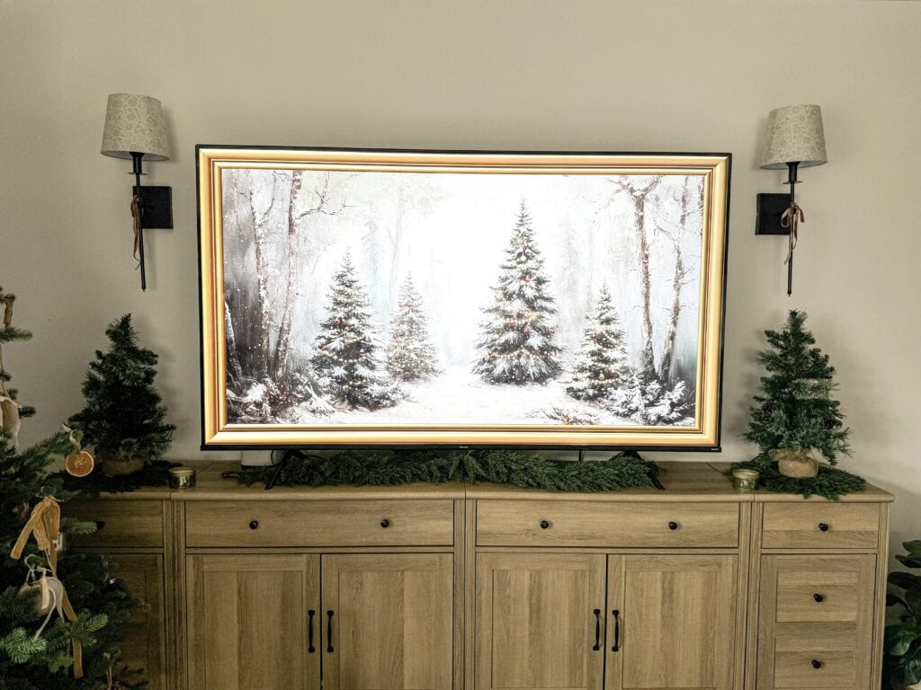 Christmas holiday scene with holiday trees, a winter forest landscape TV frame, and cozy decor in a living room setting.