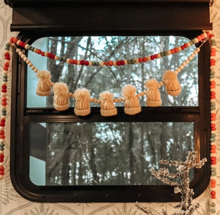Colorful bead garland with tassels hanging on a window with a winter forest view, decorative home accent from A Hundred Affections.
