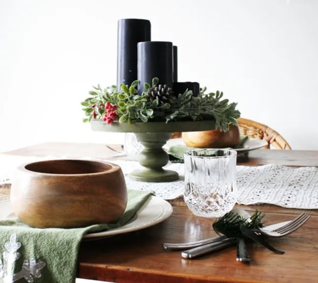 Aesthetic holiday table centerpiece with black candles, greenery, and festive accents for cozy seasonal decor.