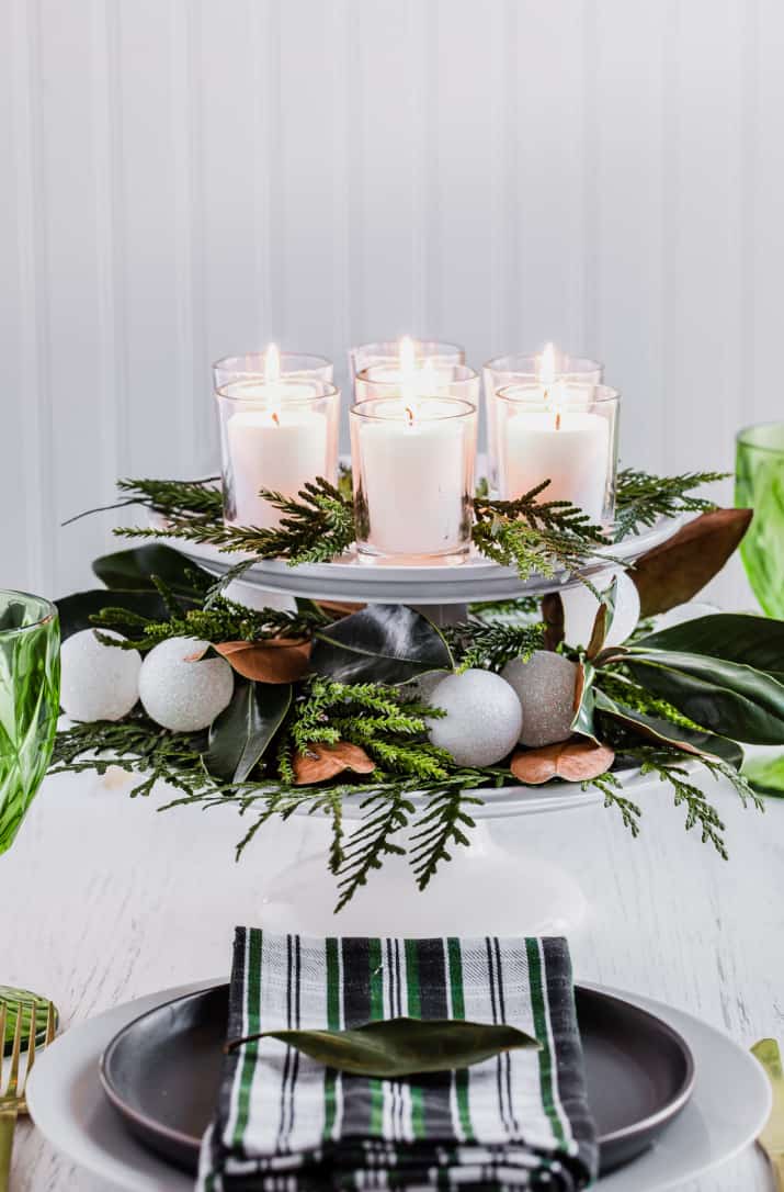 Elegant holiday table centerpiece with glowing candles and festive greenery for Christmas celebration.