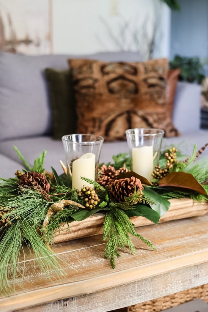 Rustic holiday centerpiece with pine cones, candles, and greenery on wooden table, perfect for seasonal home decor and festive celebrations.