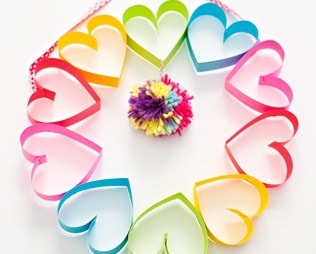 Colorful paper hearts arranged in a circle with a flower pom-pom center, showcasing DIY love crafts and creative gift ideas for special occasions.