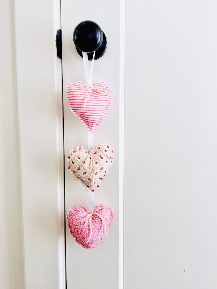 Decorative heart pillows in pink, white, and floral patterns hanging on a door handle, ideal for adding a charming, romantic touch to your home decor.