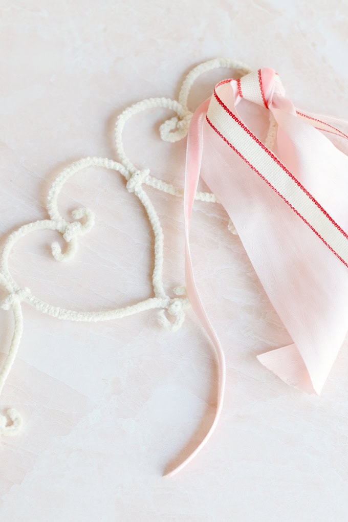 Elegant heart-shaped crochet frame with soft pink ribbon and bow, perfect for romantic and wedding decorations, expressing love and affection.