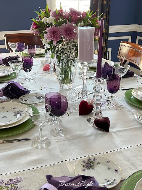Beautifully arranged formal dining table featuring purple glassware, candles, and a vibrant floral centerpiece.