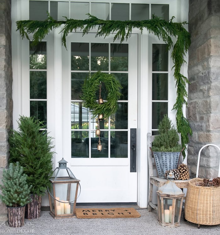 Beautiful festive front door with wreath, greenery, candles, and rustic holiday accents.