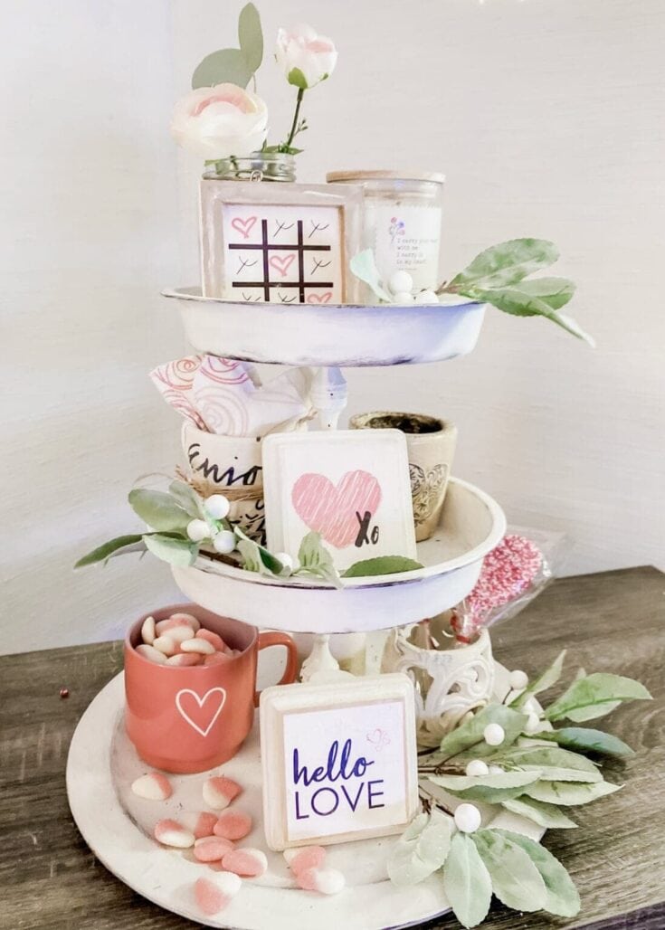 A tiered Valentine's-themed display featuring pink and white accents, heart motifs, flowers, and love-themed signs, perfect for romantic celebrations.