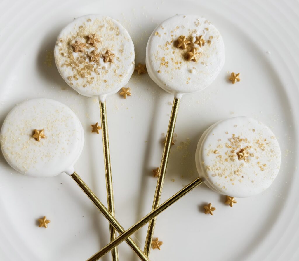 Delicious white cake pops decorated with gold star sprinkles and elegant gold sticks, perfect for weddings, parties, or special occasions.