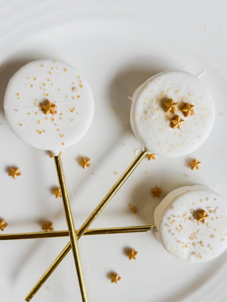 Delicious cake pops decorated with white chocolate, gold stars, and sprinkles, served on a white platter.