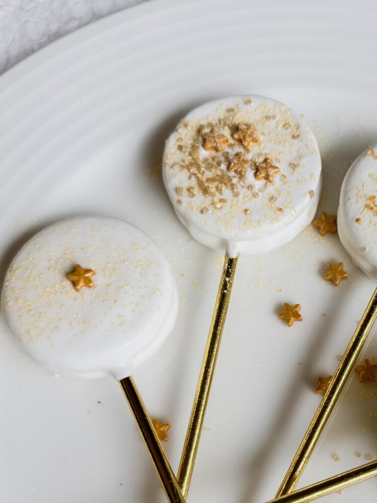 Decadent white chocolate lollipops adorned with gold star sprinkles and edible glitter, ideal for festive occasions and special desserts.