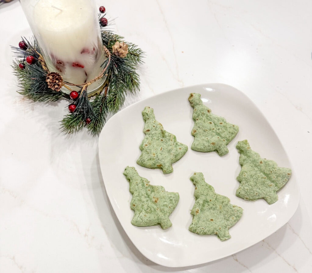 Festive matcha cookies shaped like Christmas trees on white dish with holiday candle decoration, perfect for Christmas treats and festive baking.