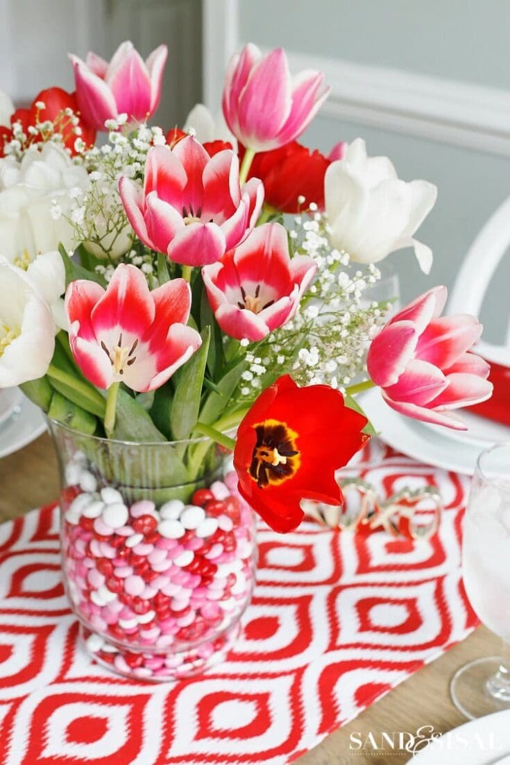 Close-up of vibrant pink, white, and red tulips arranged in a glass vase with decorative candy beads and baby's breath, perfect for spring decor and floral arrangements.