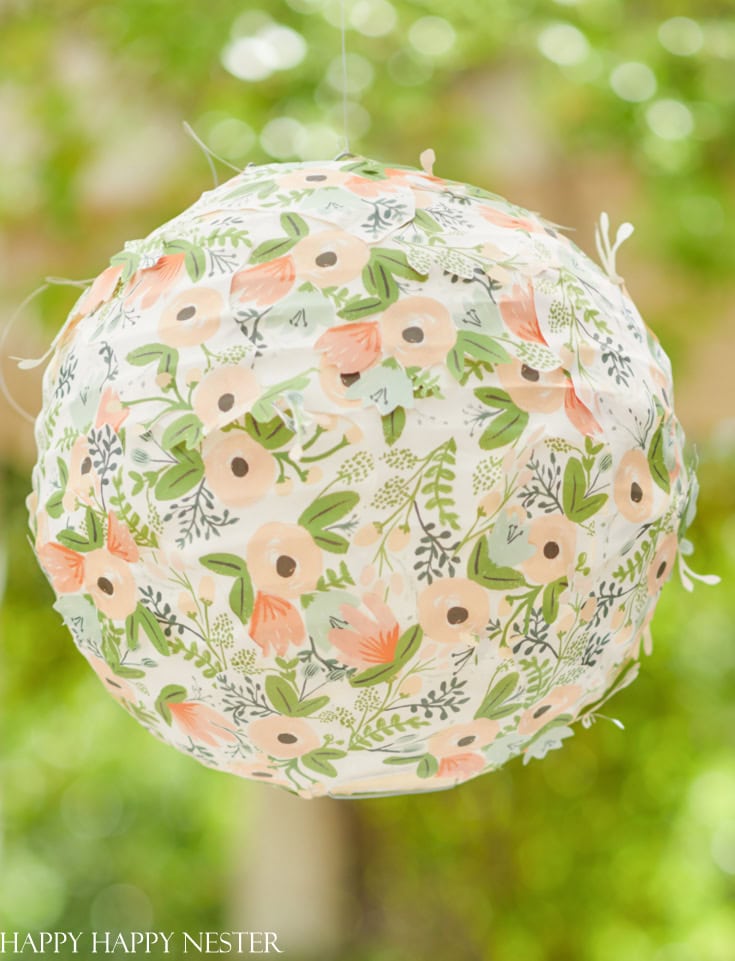 Vibrant floral print paper lantern softly illuminated with greenery background, perfect for outdoor garden party or wedding decorations.