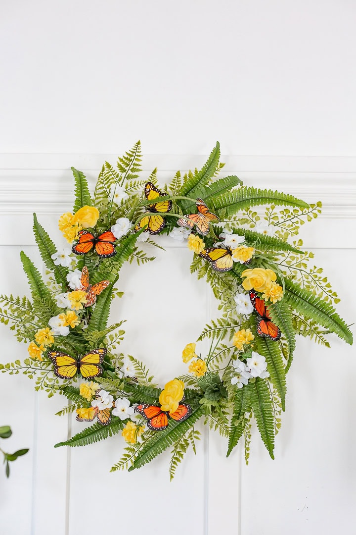 Beautiful butterfly floral wreath with yellow and white flowers and lush green ferns, perfect for home decor or spring celebrations.