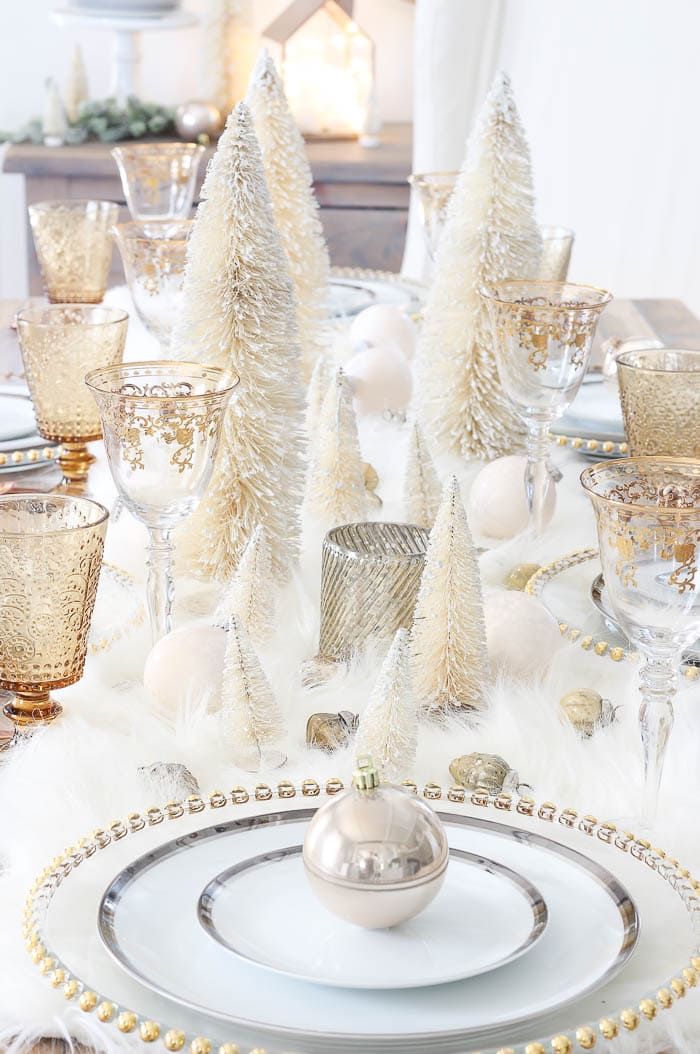 Luxurious Christmas table decor featuring white Christmas trees, gold-rimmed glasses, and metallic ornaments, perfect for festive celebrations and holiday gatherings.