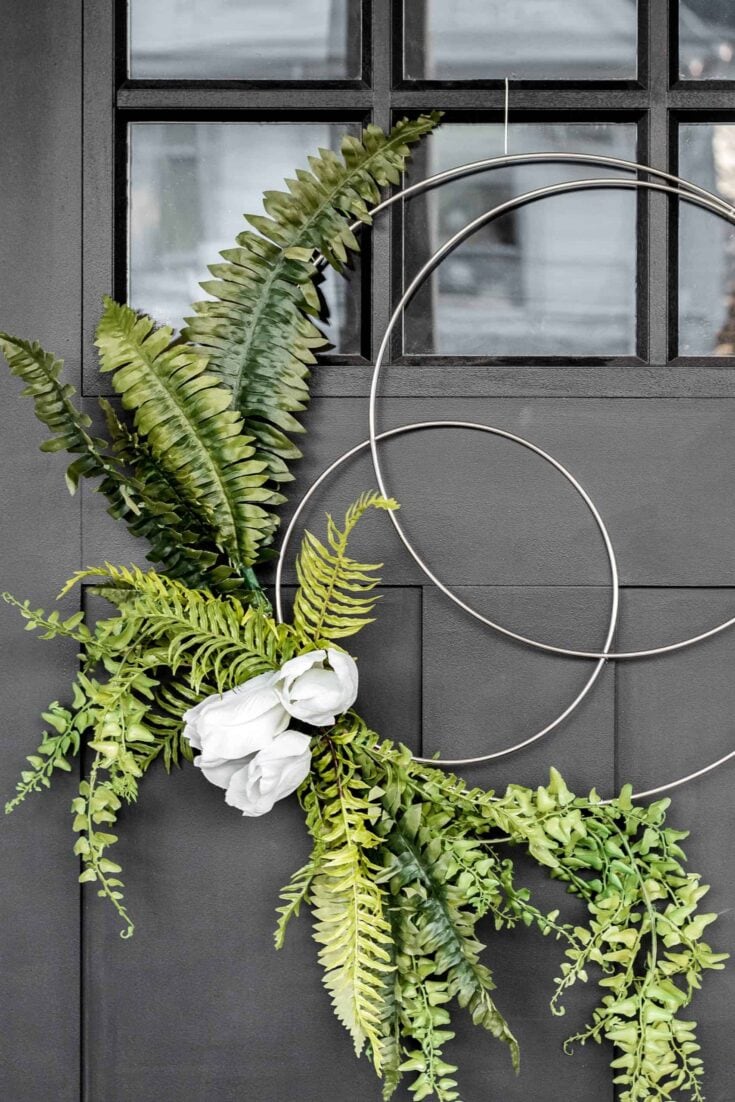 A stylish wall arrangement featuring lush green ferns and white flowers with metallic hoop accents on a dark gray wall, perfect for contemporary floral decor.