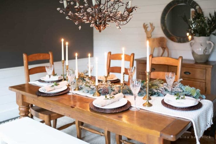 A beautifully decorated holiday dining table featuring candles, greenery, and elegant place settings for Christmas celebration.