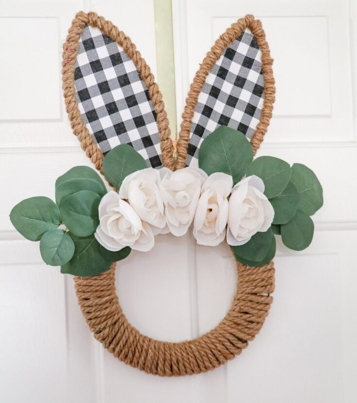 Delightful bunny-shaped door hanging decor featuring faux white flowers, eucalyptus leaves, and checkered fabric ears, perfect for spring or Easter celebrations.