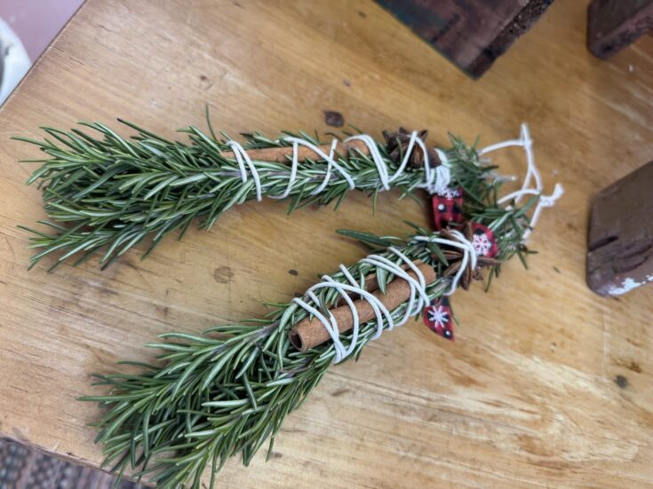 Fresh rosemary herb tied with white string, accented with cinnamon sticks and holiday ribbon, ideal for rustic Christmas decor or culinary use.