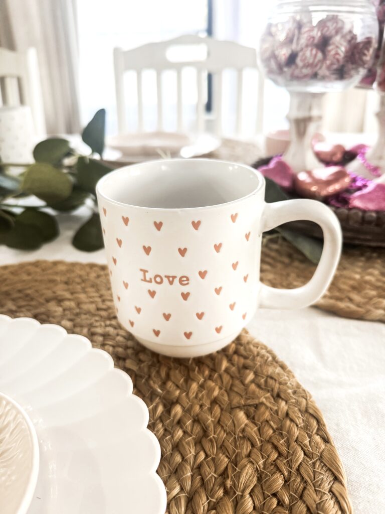 A charming white ceramic mug decorated with small pink hearts and the word "Love" in the center, perfect for romantic coffee or tea moments.