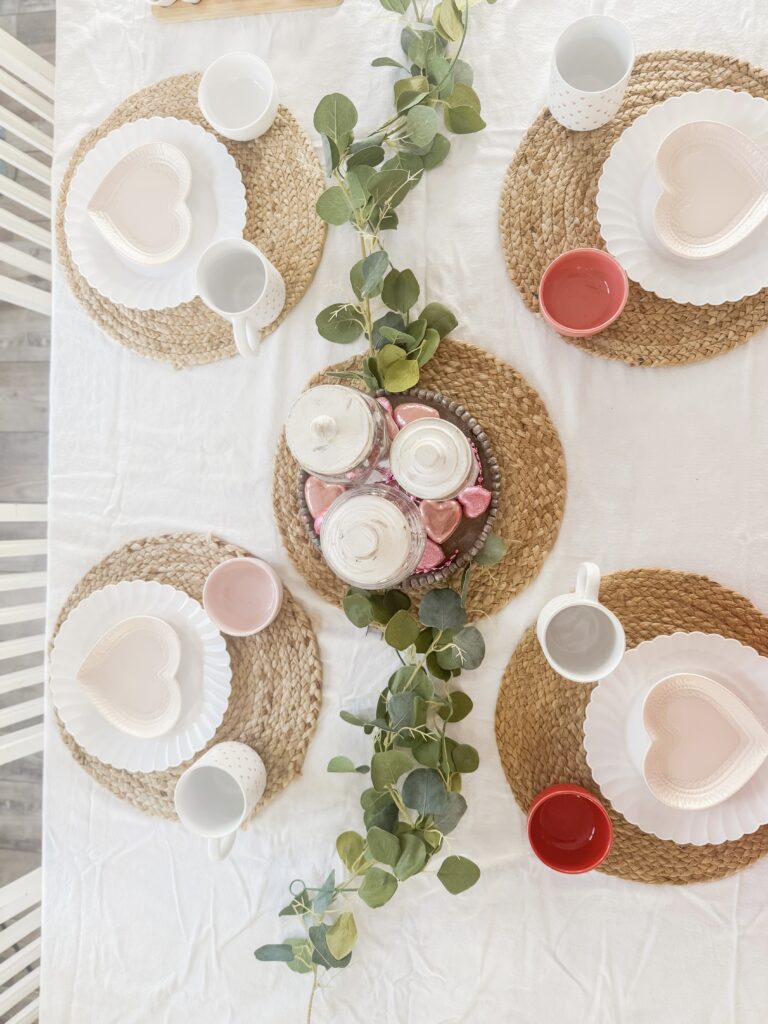 Romantic table arrangement featuring heart-shaped plates, colorful mugs, and greenery for special occasions.