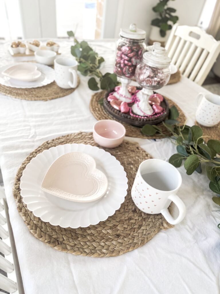 A beautifully decorated Valentine's Day table featuring heart-shaped plates, mugs with love-themed prints, pink candies, and romantic decor, ideal for special celebrations.
