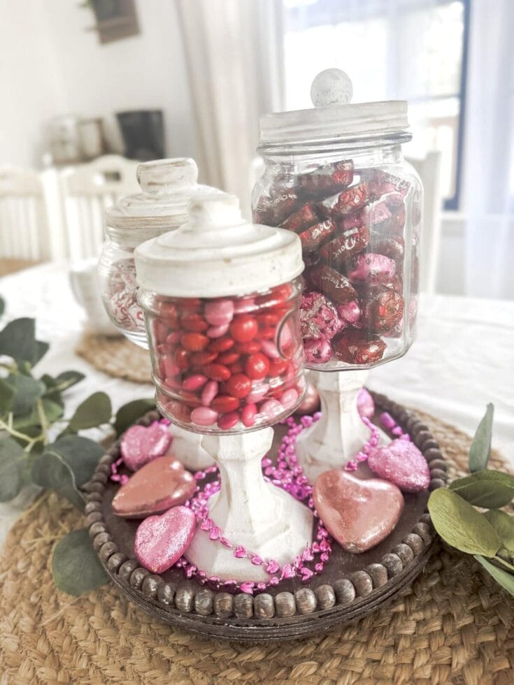 Vibrant pink and red chocolates in glass jars for Valentine's Day, decorated with pink hearts and beads, perfect for romantic gift ideas.