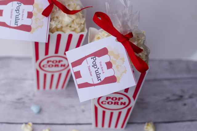 Delicious popcorn packaged in striped red and white containers with a "popcorn" label, tied with red ribbons for a charming, gift-ready presentation.