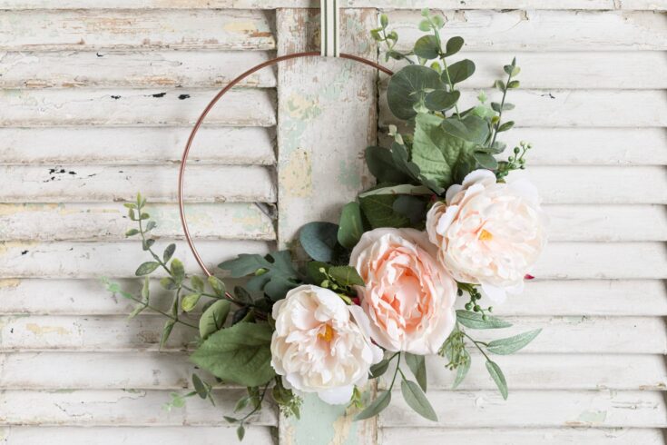 Beautiful floral wreath featuring peach roses, eucalyptus, and green foliage with a copper hoop, perfect for weddings or home decor.