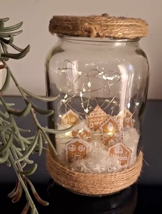 A festive glass jar filled with gingerbread house cookies, fairy lights, and holiday accents, decorated with rustic jute wrapping for a cozy holiday aesthetic.