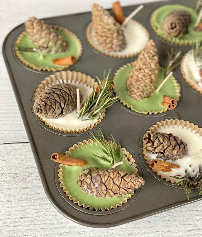 White and green pinecone candles with cinnamon sticks, rosemary, and cozy fall decor in cupcake liners, perfect for holiday table settings.