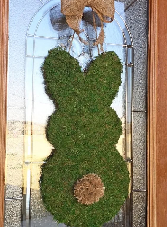 A charming moss-covered bunny-shaped hanging decoration with a burlap bow on top, perfect for spring or Easter-themed home decor, adding rustic charm and a touch of nature.