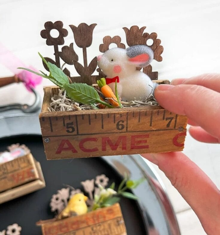 Adorable bunny figurine holding a tiny carrot in a flower box with wooden floral decor, perfect for spring or Easter decoration, handmade gift, rustic wooden planter, and whimsical garden décor.