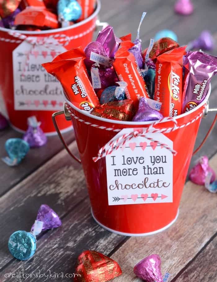 A festive red bucket filled with assorted chocolates, decorated with a heartfelt "I love you more than chocolate" note, perfect for expressing love and affection.