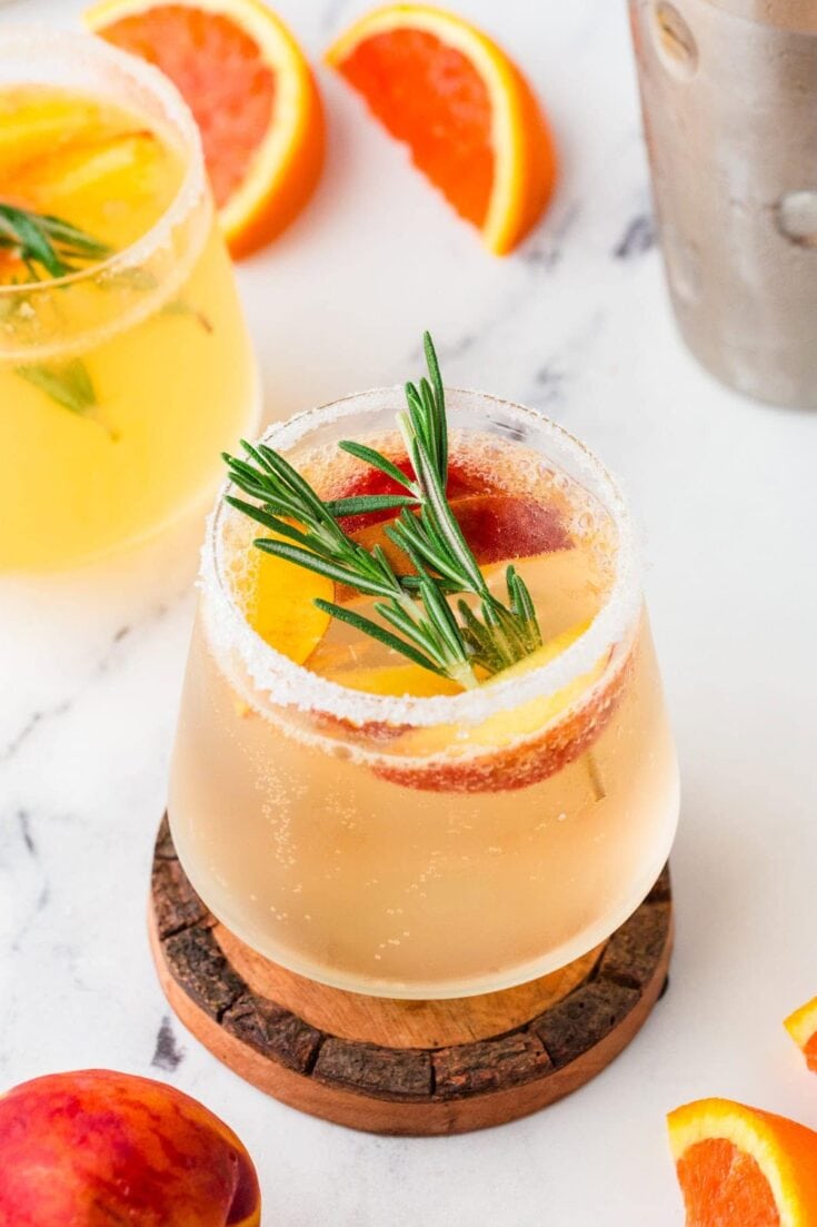 A vibrant citrus cocktail garnished with fresh rosemary, featuring slices of orange and grapefruit for a colorful, summery drink perfect for gatherings.