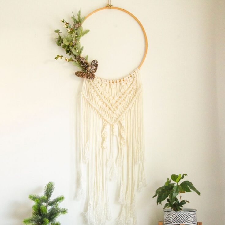 A beautifully crafted macrame wall hanging decorated with green foliage and pine cones, perfect for bohemian-inspired interior design and wall art.