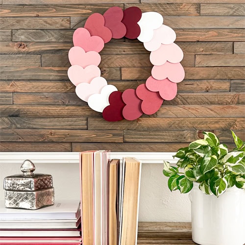 Vibrant pink and red paper heart garland hanging on a rustic wooden wall, perfect for home decor, romantic celebrations, or Valentine’s Day. Adds warmth and love to any space.