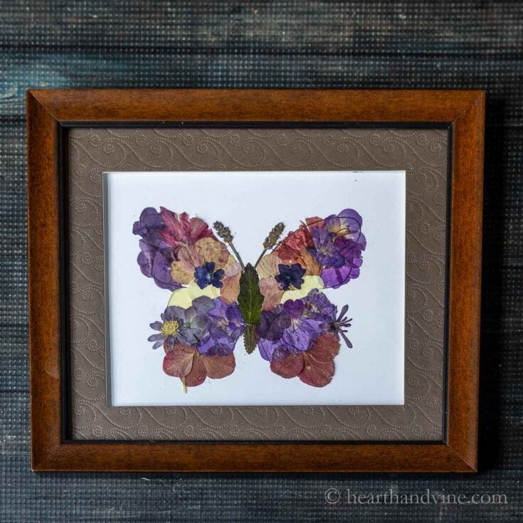 A framed butterfly artwork created with pressed colorful flowers and leaves, showcasing botanical pressed flower art for home decor and nature-inspired wall art.