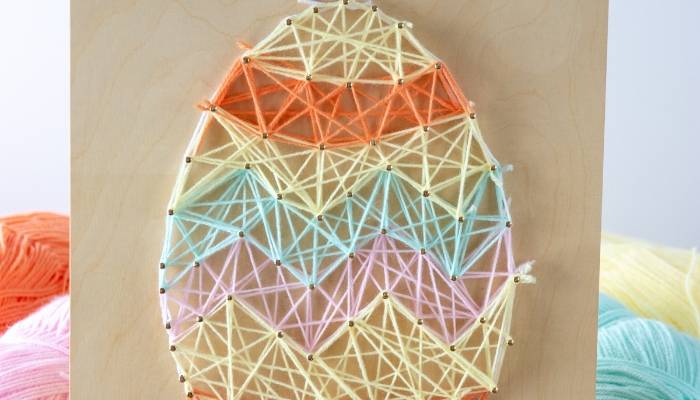 Brightly colored yarn egg art with intricate string geometric pattern, perfect for spring or Easter decor, handmade craft project.