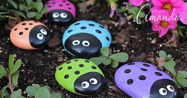 Brightly painted ladybug rocks arranged on soil with small green plants, perfect for garden decor, crafts, and outdoor ornaments.