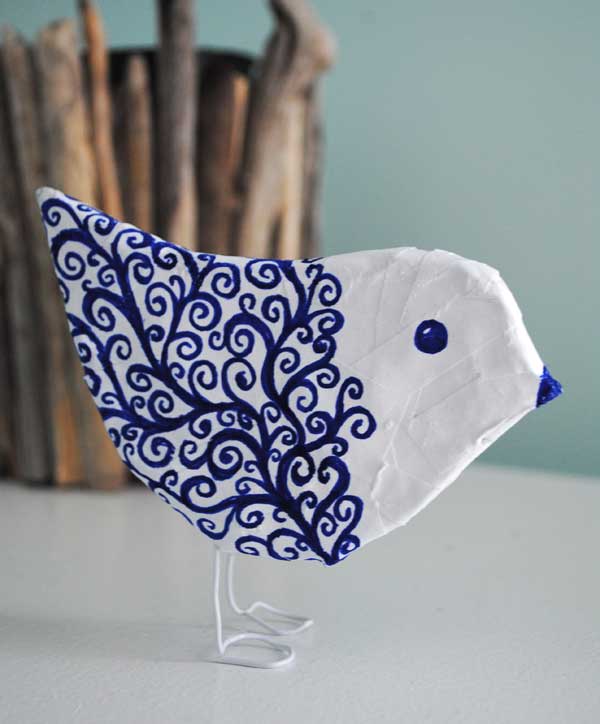 A decorative craft bird made of paper with detailed blue swirl patterns and a simple white stand for display.