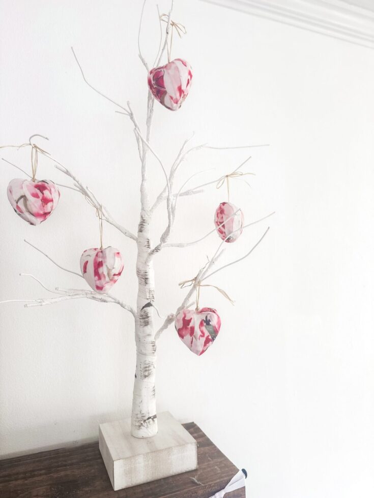 Decorative white tree with pink and red heart-shaped ornaments hanging from its branches, placed on a wooden surface for home decor or romantic-themed events.