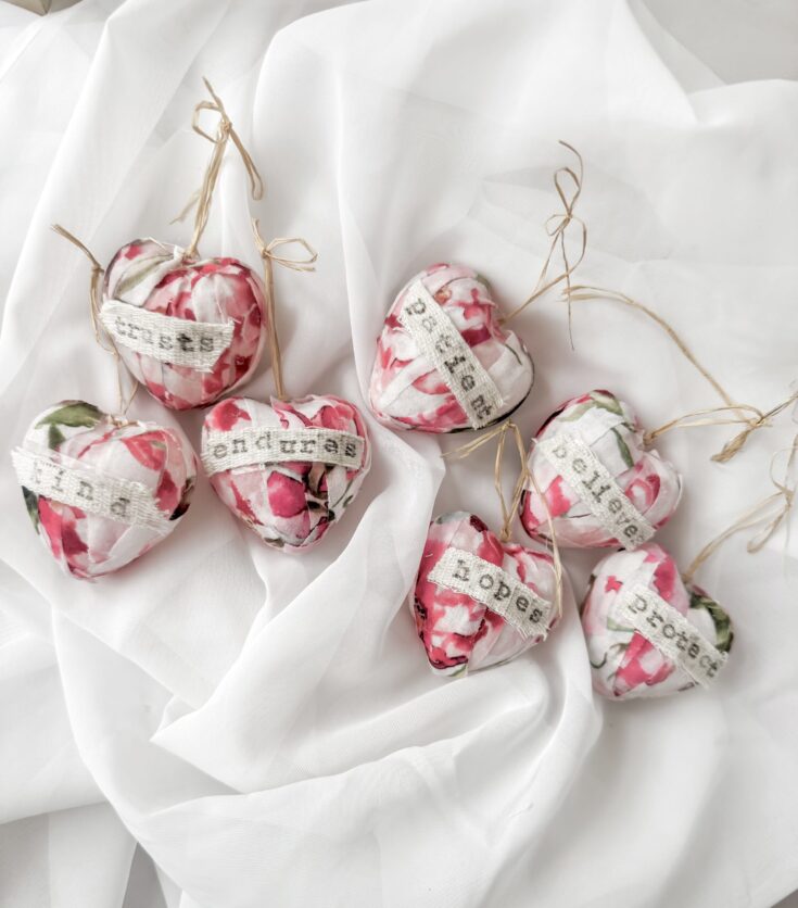 Set of handmade fabric heart ornaments with words like 'endurance' and 'hope' on white and pink marbled fabric, tied with natural twine, perfect for Valentine's Day decor.