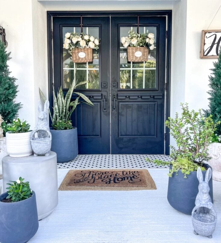 Elegant black double front door decorated with white floral arrangements in hanging baskets, surrounded by potted plants and garden ornaments, creating a welcoming and stylish entrance.