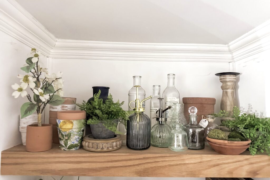 Elegant display of glass bottles, potted plants, and decorative items on a wooden shelf, creating a charming and natural home decor aesthetic.