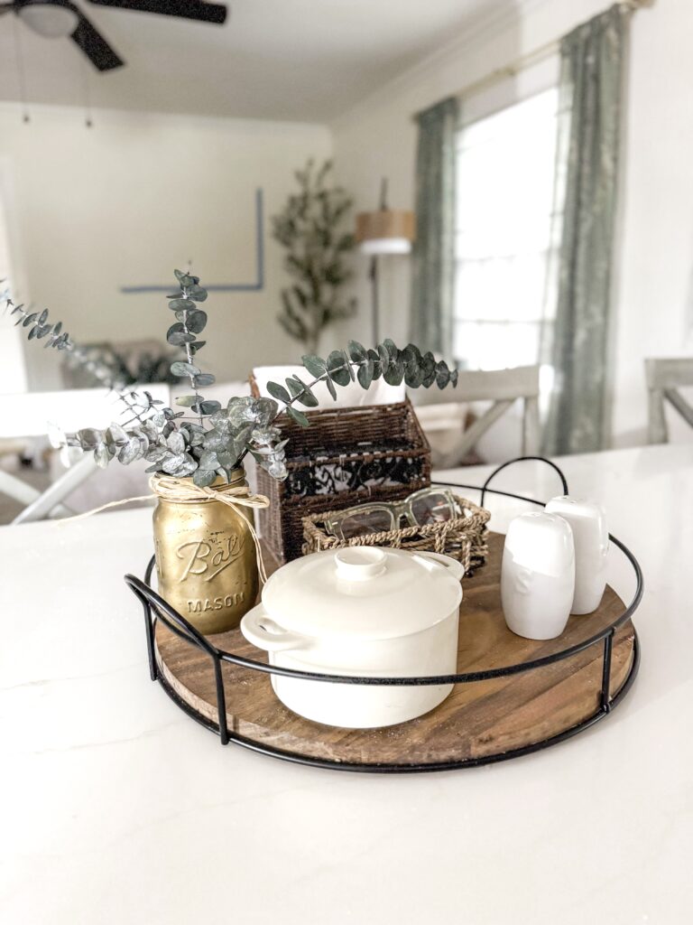 A decorative tray featuring a white ceramic pot, a gold Mason jar with eucalyptus, and other stylish kitchen accessories, creating a cozy and modern home ambiance.
