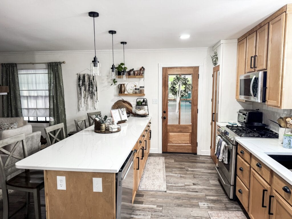 Bright and inviting kitchen featuring wooden cabinets, a large white island, stainless steel appliances, and natural light from windows, perfect for family cooking and gatherings.