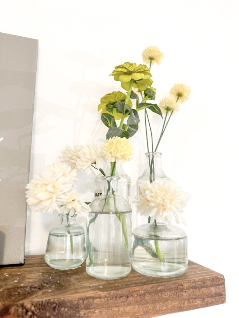 Beautiful white and yellow flowers displayed in clear glass vases on a rustic wooden surface, creating a charming and fresh floral decor scene.